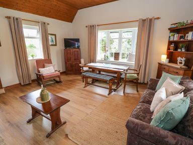 A living room with wooden furniture a sofa with cushions a coffee table a TV on a cabinet and a dining table with chairs and a bench at Aggrafard in Oughterard County Galway