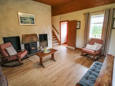 A living room with wooden rocking chairs a wooden coffee table a stove fireplace staircase and a window with curtains at Aggrafard in Oughterard County Galway