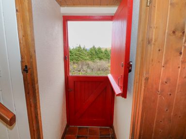 An interior view of a small vestibule with a red stable door partially open showing greenery outside at Aggrafard in Oughterard County Galway