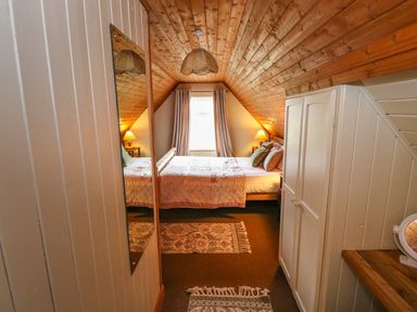 A bedroom with a wooden ceiling a bed two bedside tables with lamps and a window with curtains at Aggrafard in Oughterard County Galway