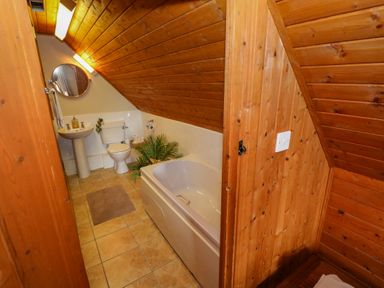 A bathroom with a bathtub toilet sink round mirror and wooden walls at Aggrafard in Oughterard County Galway