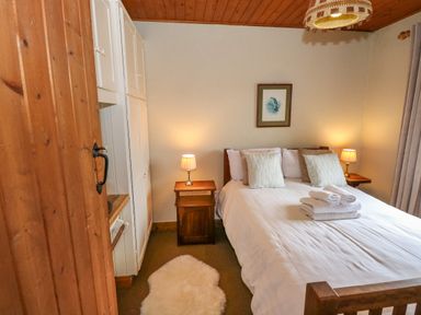 A bedroom with a bed with pillows and folded towels bedside tables with lamps a rug on the floor and built in cupboards at Aggrafard in Oughterard County Galway