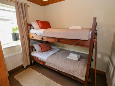 A bedroom with a wooden bunk bed a window with curtains and a lamp on a radiator at Aggrafard in Oughterard County Galway