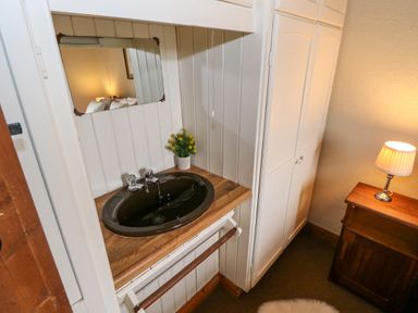 A corner with a black sink on a wooden countertop a mirror a small plant a white cupboard and a wooden nightstand with a lit lamp at Aggrafard Oughterard County Galway