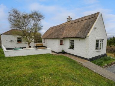 A white cottage with a thatched roof and a small courtyard with a bench and tree at Aggrafard in Oughterard County Galway