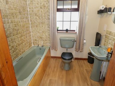 A bathroom with a bathtub toilet and sink with beige curtains on a window at Corrib Near Oughterard County Galway
