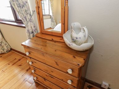 A wooden dresser with a mirror and a ceramic pitcher and basin near a window with floral curtains at Corrib Near Oughterard County Galway