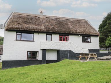 A thatched roof house with white and black walls and a wooden picnic table on the grass at Corrib Near Oughterard County Galway