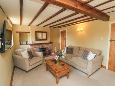 A living room with a sofa an armchair a wooden coffee table a fireplace and a wall-mounted television at Tillers Cottage in Ebberston