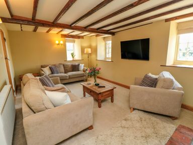 A living room with beige sofas a wooden coffee table a wall-mounted TV and exposed wooden ceiling beams at Tillers Cottage in Ebberston