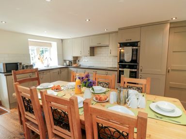 A kitchen with wooden dining table set for breakfast with plates croissants and juice at Tillers Cottage in Ebberston