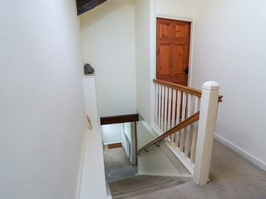 A staircase with beige carpet leading down to a door with a wooden railing and a closed wooden door at the top at Tillers Cottage in Ebberston