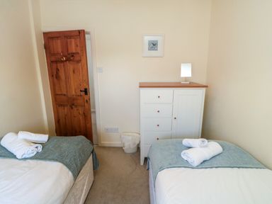 A bedroom with two single beds a white cabinet and a wooden door at Tillers Cottage in Ebberston
