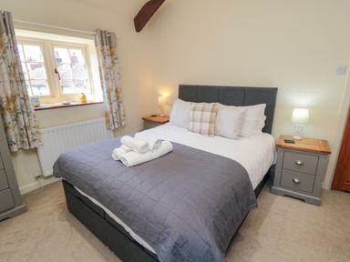 A bedroom with a double bed with gray bedding two bedside tables with lamps and a window with patterned curtains at Tillers Cottage in Ebberston