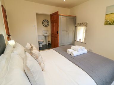 A bedroom with a bed, pillows, folded towels, a wardrobe, a window, and an en suite bathroom at Tillers Cottage in Ebberston