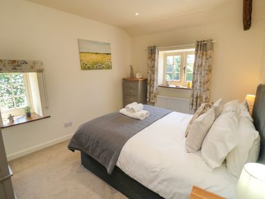 A bedroom with a bed with rolled towels on the bed a chest of drawers and two windows with curtains at Tillers Cottage in Ebberston