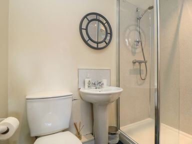 A bathroom with a toilet, pedestal sink, round mirror, and a glass-enclosed shower at Tillers Cottage in Ebberston