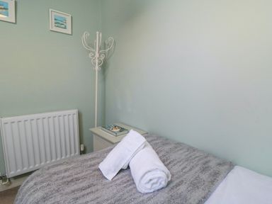 A bedroom corner with a bed covered by a gray blanket and white towels on top a white coat rack and two small framed pictures above a radiator at Tillers Cottage in Ebberston