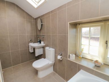 A bathroom with a toilet sink mirror window blinds and toiletries at Tillers Cottage in Ebberston