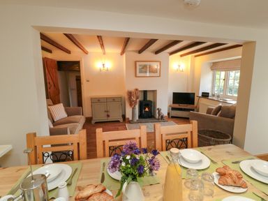 A kitchen dining table set with plates croissants and juice in an open plan living room with sofas a stove and television at Tillers Cottage in Ebberston