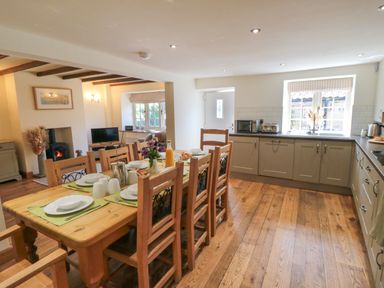 A kitchen and dining area with wooden table set for meal and kitchen cabinets at Tillers Cottage in Ebberston