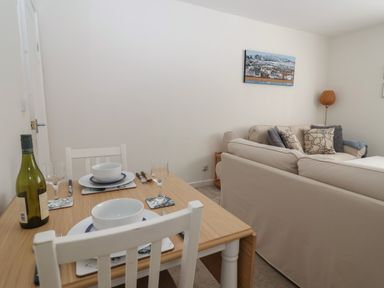 A small dining table set for two with bowls and wine glasses next to a beige sofa with cushions in a living room at 16 Church Street in Lyme Regis
