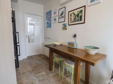 A kitchen area with a wooden table holding bowls and a radio stools underneath and framed pictures on the wall at 16 Church Street Lyme Regis
