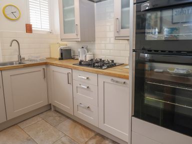 A kitchen with white cabinets wooden countertops a gas stove a double oven a sink and a wall clock at 16 Church Street Lyme Regis