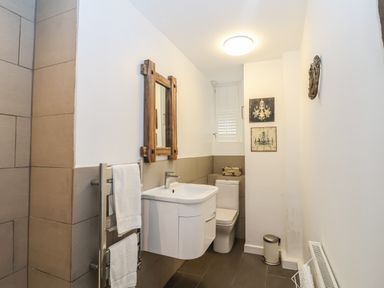 A bathroom with a wooden mirror above a white sink and a toilet next to a small window at 16 Church Street in Lyme Regis