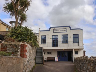 Exterior view of a white building with blue doors and windows labeled Marine Theatre with stone walls and plants in front at 16 Church Street Lyme Regis