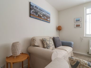 A living room with a beige sofa cushions a side table with a woven lamp floor lamp and coastal paintings on the walls at 16 Church Street in Lyme Regis