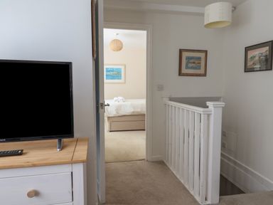 A hallway with a TV on a wooden stand and a view into a bedroom with a bed and artwork at 16 Church Street Lyme Regis