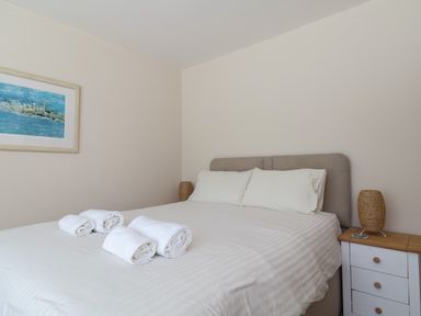 A bedroom with a double bed white linens rolled towels bedside table and framed painting at 16 Church Street in Lyme Regis