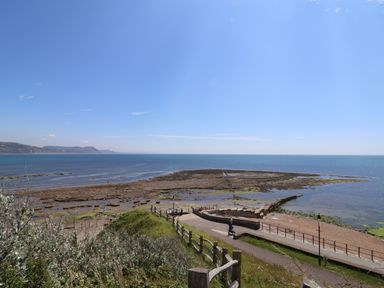 A coastal view with a pathway, wooden fence, rocky shore, and sea at 16 Church Street in Lyme Regis