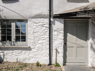 Exterior of a white stone cottage with a window and a door with a black drainpipe between them at Sunrise Cottage St Kew Highway near Wadebridge