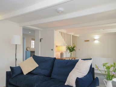 A living room with a blue sofa and cushions a floor lamp a table lamp and flowers at Sunrise Cottage in St Kew Highway near Wadebridge
