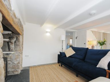A living room with a stone fireplace a blue sofa a floor lamp and a woven rug at Sunrise Cottage in St Kew Highway near Wadebridge