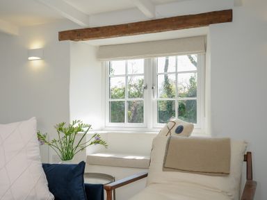 A seating area with cushions and flowers by a window with wooden beam at Sunrise Cottage in St Kew Highway near Wadebridge