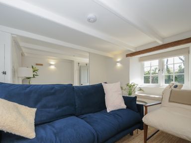 A living room with a blue sofa beige armchair window and flowers at Sunrise Cottage St Kew Highway near Wadebridge