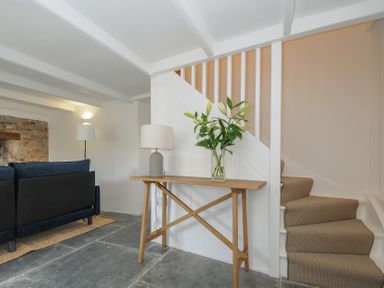 A wooden console table with a lamp and flowers next to carpeted stairs in a living area at Sunrise Cottage in St Kew Highway near Wadebridge