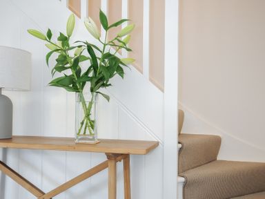 A wooden table with a glass vase of lilies and a lamp beside a carpeted staircase at Sunrise Cottage in St Kew Highway near Wadebridge