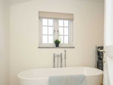 A bathroom with a freestanding bathtub below a window with a potted plant and a towel on the tub at Sunrise Cottage in St Kew Highway near Wadebridge