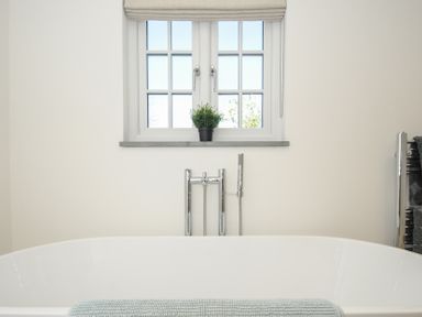 A bathroom with a white bathtub under a window with a plant on the windowsill at Sunrise Cottage in St Kew Highway near Wadebridge