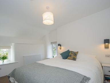 A bedroom with a large bed two pillows two windows a bedside table and a ceiling light at Sunrise Cottage St Kew Highway near Wadebridge