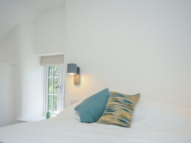 A bed with two pillows next to a window and a wall lamp at Sunrise Cottage in St Kew Highway near Wadebridge