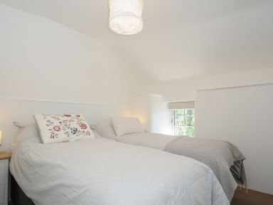 A bedroom with two single beds and a small window at Sunrise Cottage in St Kew Highway near Wadebridge