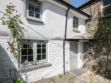 The exterior of a white cottage with windows and a door labeled Sunrise Cottage at St Kew Highway near Wadebridge