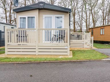 A caravan with a beige deck and two chairs outside on a paved area surrounded by grass at The Mermaid A04 in Par