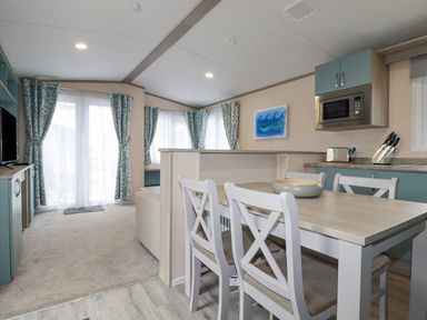 A dining area with a table and chairs next to a kitchen with blue cabinets and a microwave at The Mermaid A04 in Par