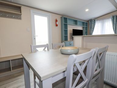 A dining table with four chairs and a bowl in a room with a TV unit and curtains at The Mermaid A04 in Par